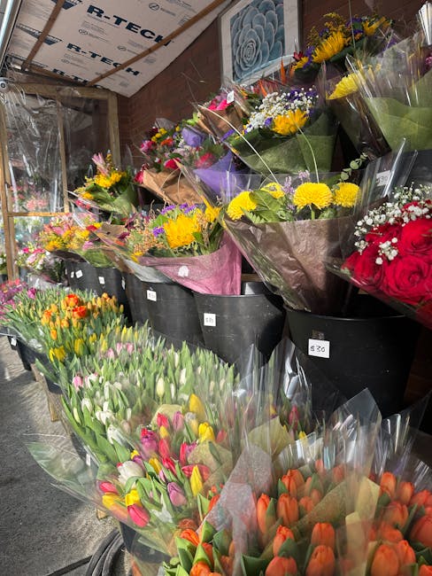 A variety of fresh floral bouquets arranged in black plastic buckets inside a floral shop. The bouquets feature a mix of brightly colored flowers including yellow chrysanthemums, purple irises, white